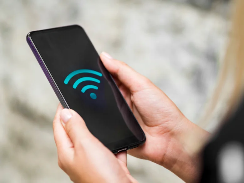 Ruka drží chytrý telefon s ikonou bezdrátového připojení.