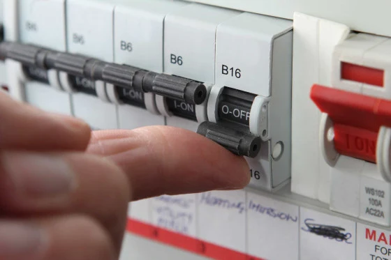 Ruka otočí vypínač jističe v elektrickém rozvaděči.