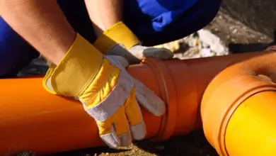 Ruce pracovníka s rukavicemi upravují oranžové tlakové potrubí.