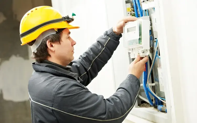 Elektrikář připojuje třífázový elektroměr do rozvaděče.
