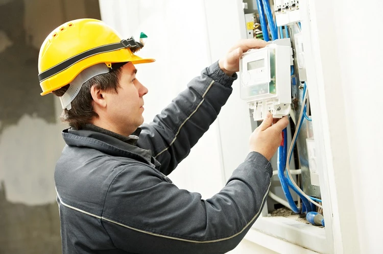Elektrikář připojuje třífázový elektroměr do rozvaděče.
