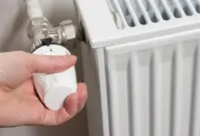 Ruka otáčí termostatem na kohoutku radiátoru pro nastavení teploty.