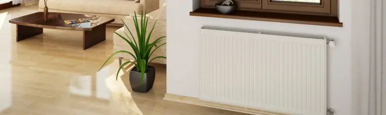 Bílý litinový radiátor pod oknem v obývacím pokoji