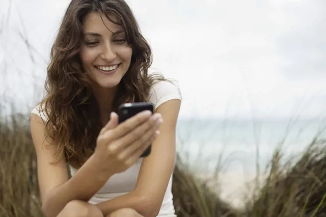 Žena se usmívá při používání mobilního telefonu u moře.