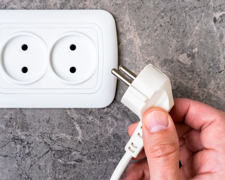 Ruka drží zástrčku u elektrické zásuvky na dlažbě v koupelně.