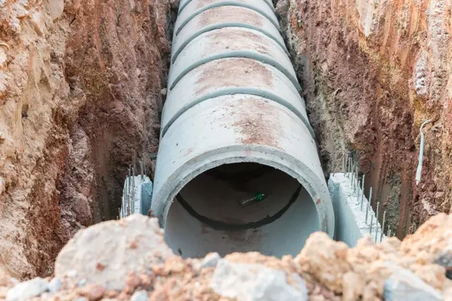Velká betonová tlaková kanalizační trubice v zemi.