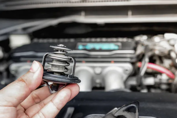 Ruka drží termostat nad otevřeným motorem automobilu.