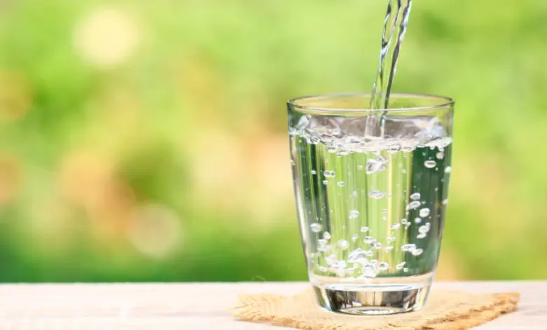 Voda se nalévá do sklenice na venkovním pozadí.