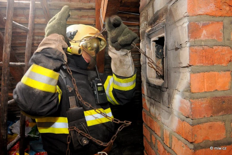 Hasič s řetězem u komína při zásahu