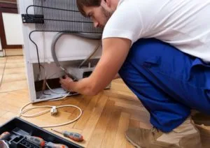 Technik opravuje ledničku s použitím nástrojů na podlaze.