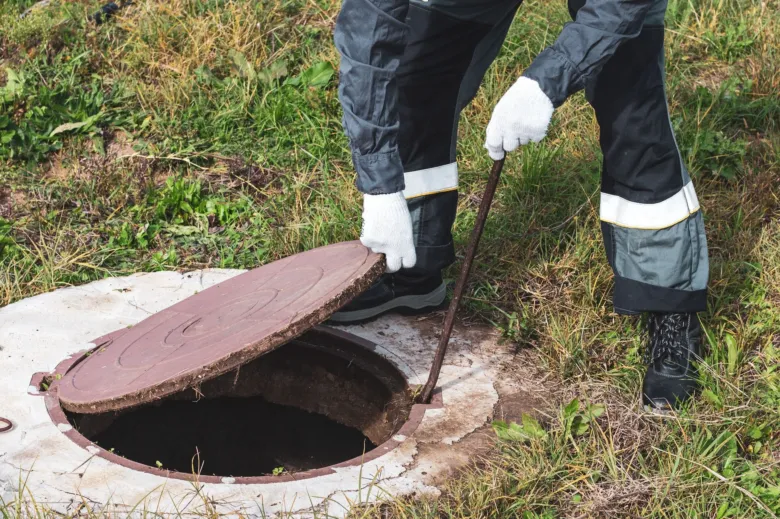 Pracovník zavírá víko septiku pomocí páky v bezpečné výšce.