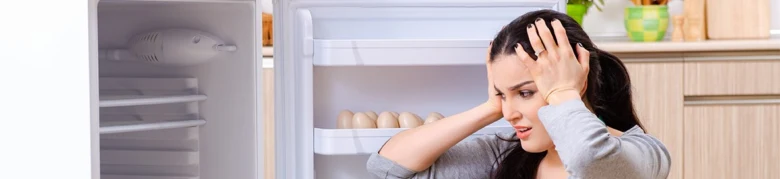 Žena stojí před prázdnou lednicí s kartonem vajec.