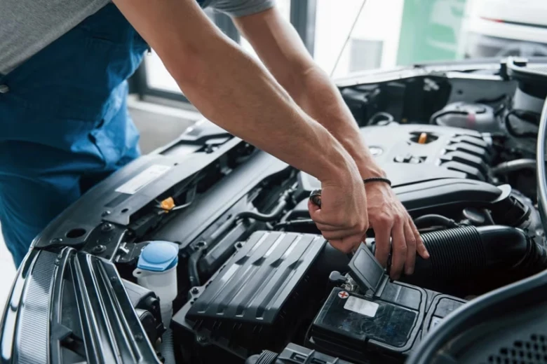 Mechanik připojuje svorky k automobilové baterii pod kapotou.