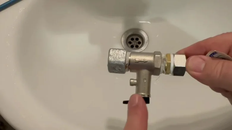 Ruční držení ventilu s únikem vody nad umyvadlem.