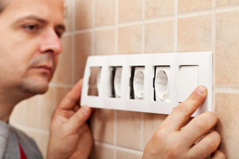 Muž montuje elektrickou zásuvku na dlažděnou stěnu v bytě.