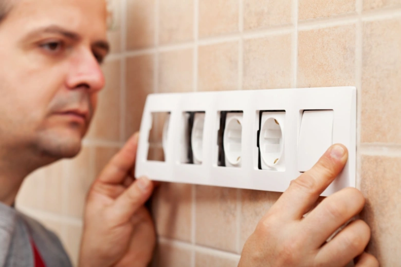 Muž montuje elektrickou zásuvku na kuchyňskou dlažděnou stěnu.