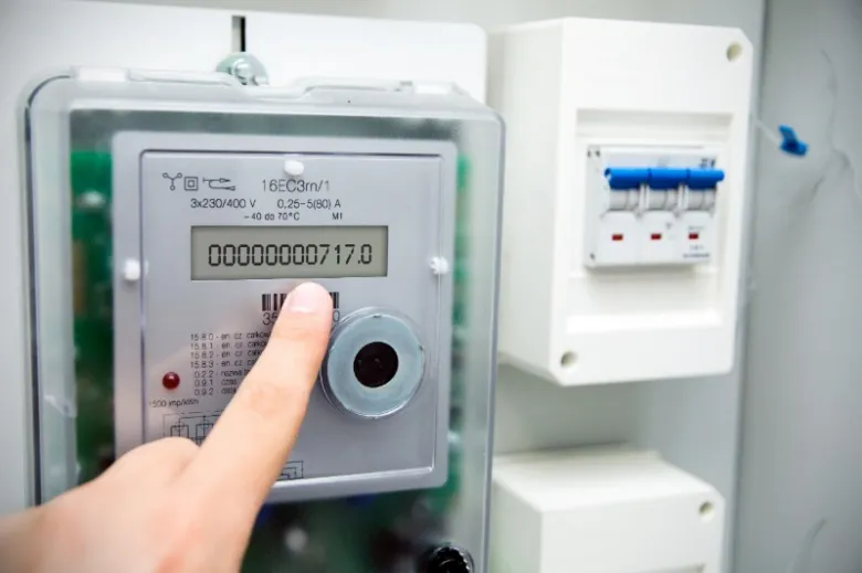 Prst ukazující na displej elektronického elektroměru s čísly a symboly.