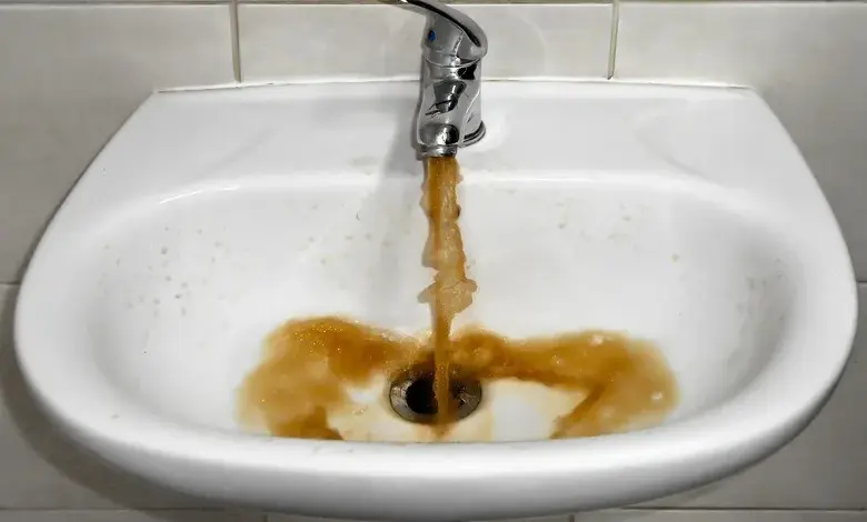 Znečištěná voda z kohoutku v umyvadle ukazuje problém s kvalitou vody.