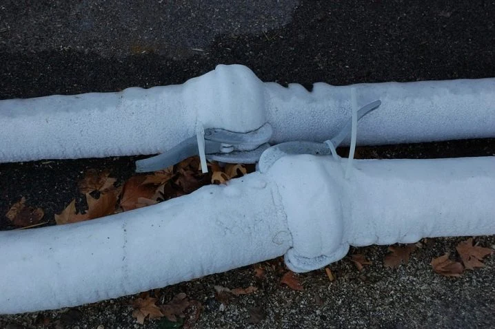 Zamrzlé plastové potrubí pokryté mrazem na zemi.