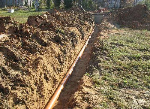 Zasazení oranžové kanalizační trubice do vykopaného příkopu pro správnou hloubku.