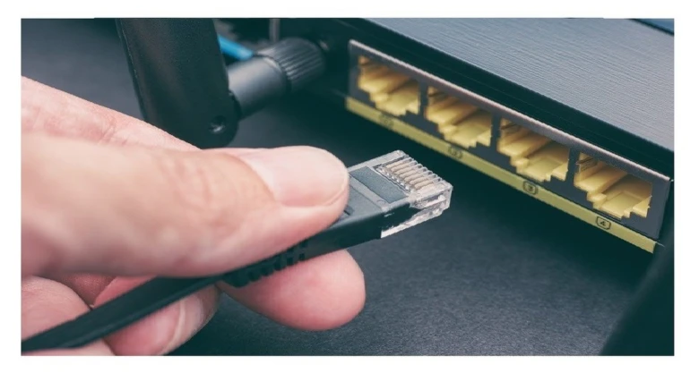 Ruka drží ethernet kabel u portů na síťovém přepínači.