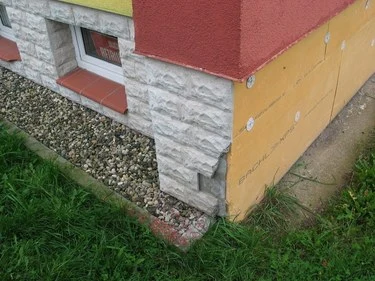 Základní sokl budovy s kamennou omítkou a žlutým izolačním panelem.
