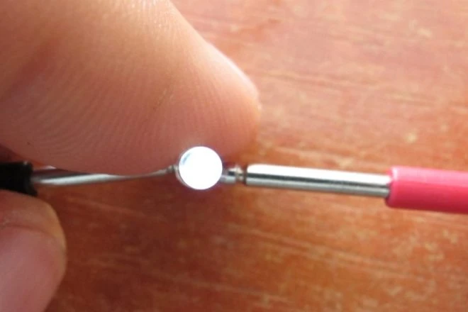 Prst drží sondu multimetru připojenou k malému elektronickému součástku.