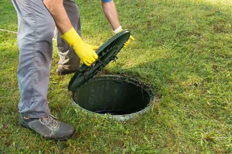 Pracovník zavírá víko septiku na trávníku s rukavicemi.