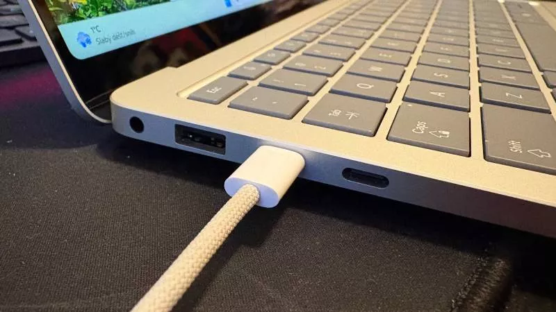 Bílý kabel nabíječky zapojen do USB-C portu notebooku.