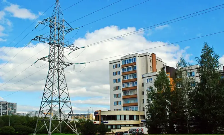 Vysoký elektrický sloup s vedením na pozadí bytových domů.