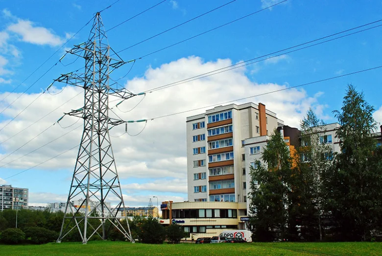 Vysoký elektrický sloup s vedením na pozadí bytových domů.