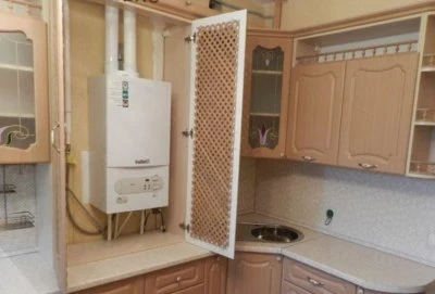 Plynový kotel maskovaný v kuchyňském skříni s dekorativní mřížkou.