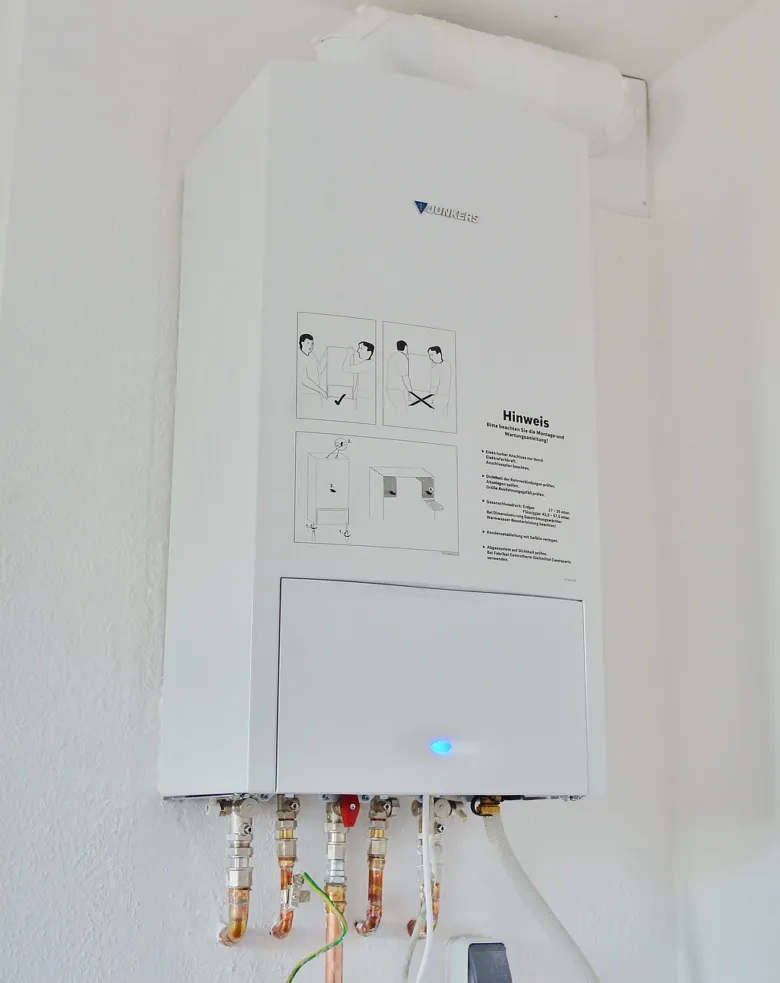 Bílý nástěnný kotel s viditelnými elektrickými vodiči.