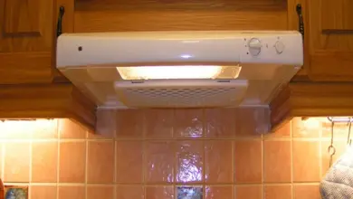 Bílá digestoř nainstalovaná pod skříňmi s viditelným elektrickým zapojením.