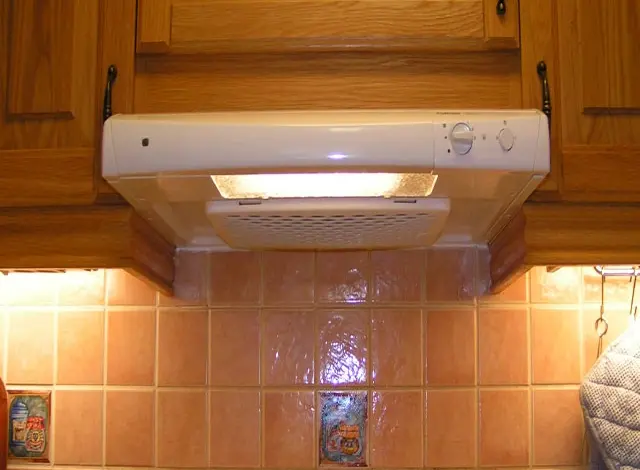 Bílá digestoř nainstalovaná pod skříňmi s viditelným elektrickým zapojením.