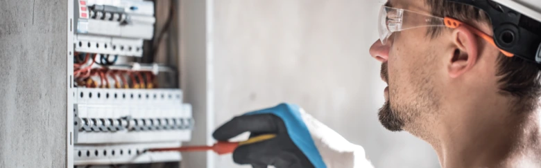 Elektrikář opravuje pojistky v rozvaděči s viditelným dráty.