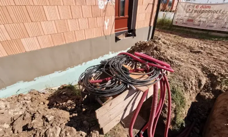 Černé kabely a červená hadice vedou v jednom výkopu u domu.