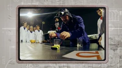 Muž v ochranném obleku ukazuje nebezpečí elektrického proudu studentům.