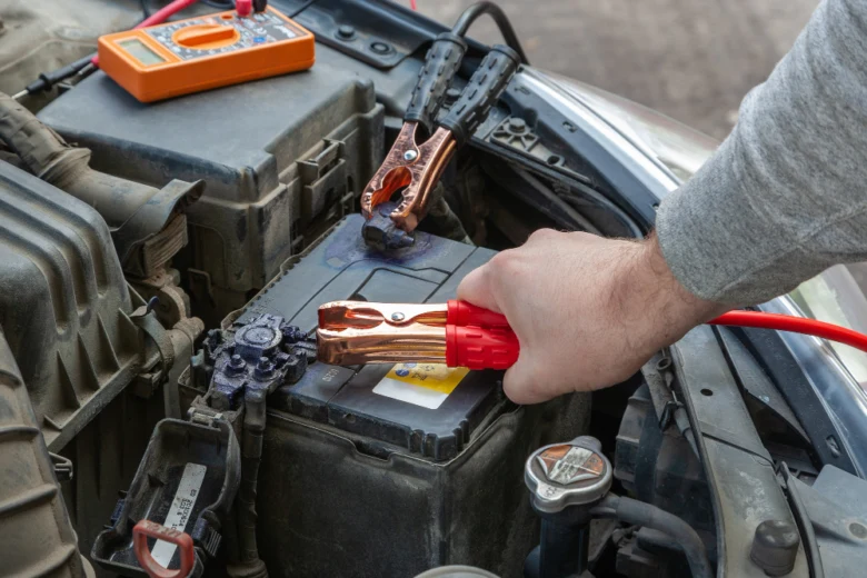 Člověk připojuje červený kabel k autobaterii pro testování napětí.