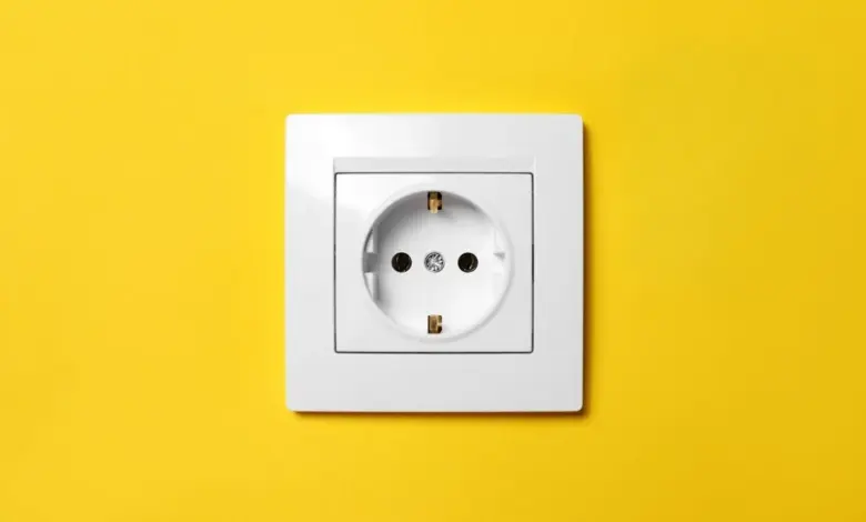 Bílá elektrická zásuvka na žluté stěně pro ilustraci spotřeby proudu.