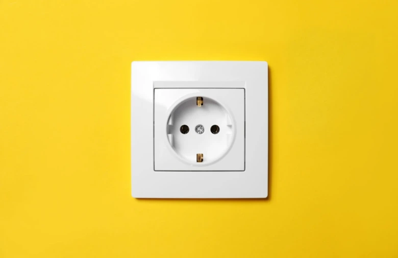 Bílá elektrická zásuvka na žluté stěně pro ilustraci spotřeby proudu.