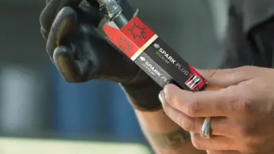 Mechanik drží novou svíčku zapalovací s viditelným štítkem.