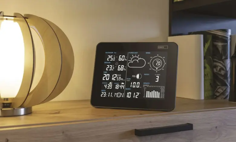 Digitální meteostanice s displejem ukazující počasí na dřevěném stole.