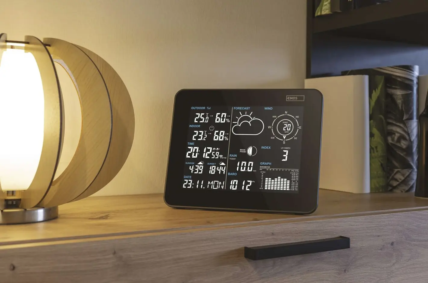 Digitální meteostanice s displejem ukazující počasí na dřevěném stole.