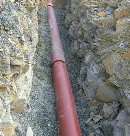 Červená kanalizační trubka v jámě pro instalaci.