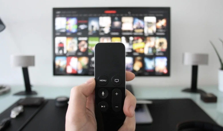 Ruka drží ovladač před televizí s nabídkou streamování.