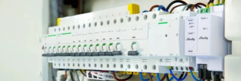 Bílá elektrická rozvaděč s měřiči a pojistkami pro třífázový systém.