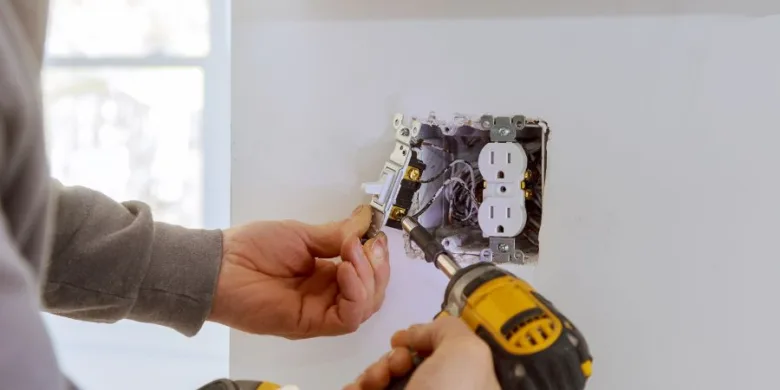 Elektrikář montuje zásuvku ve zdi s viditelnými vodiči.