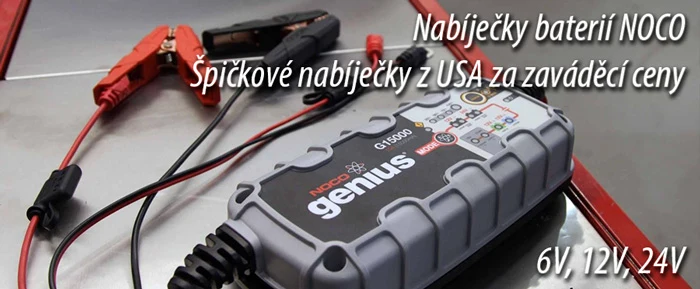 Nabíječka baterie s červenými a černými svorkami na kovové ploše.