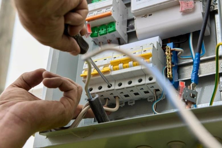 Elektrikář upravuje třífázový jistič v rozvaděči.